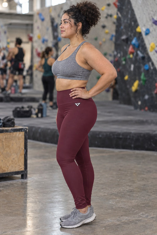 Woman wearing the Burgundy Essential High-Waisted Yoga Leggings with the Vantacore V emblem on the hip – side view showing the V emblem on the hip