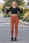 Woman wearing the Rust Essential High-Waisted Yoga Leggings with the Vantacore V emblem on the hip – front view