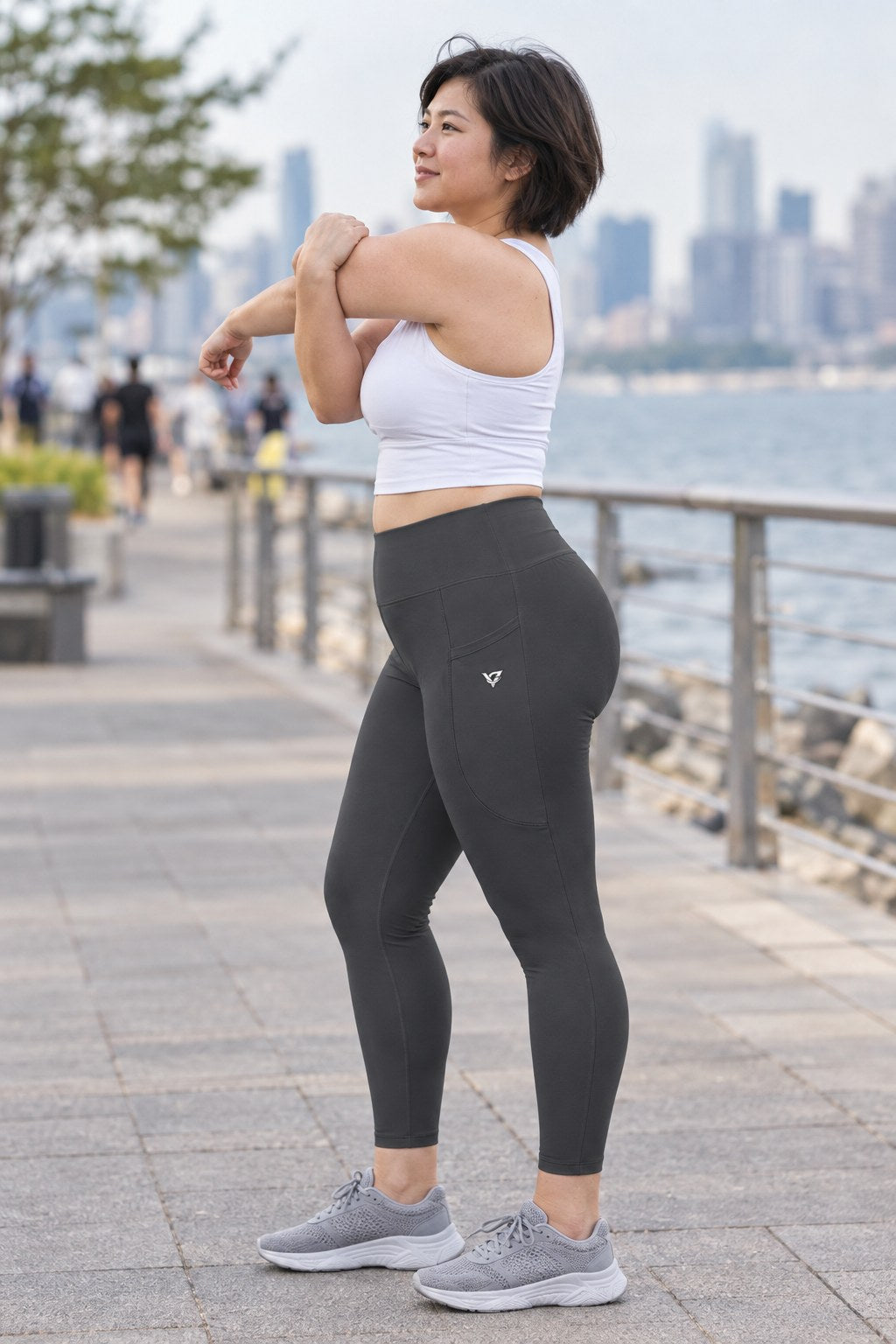 Charcoal Grey Essential leggings with pockets, AI-generated fictional adult model – side view showing the side pocket and V emblem
