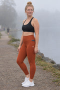 Rust Essential leggings with pockets, AI-generated fictional adult model – front three-quarter view showing the side pocket