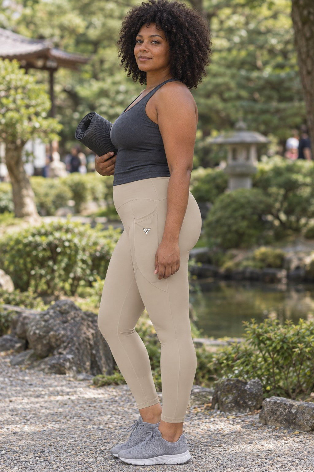 Sand Beige Essential leggings with pockets, AI-generated fictional adult model – side view showing the side pocket and V emblem