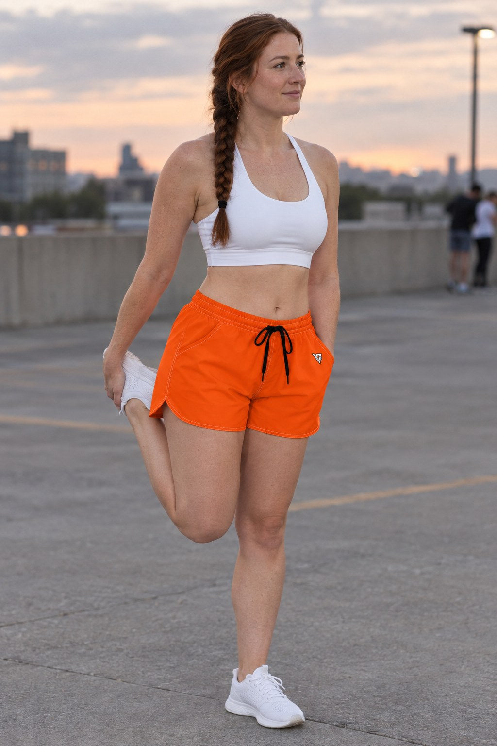 Woman wearing the Blaze Orange Essential women's athletic shorts with pockets and the Vantacore V emblem – three-quarter view showing the side pocket and V emblem