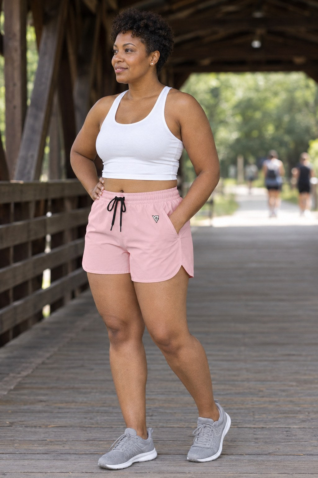 Woman wearing the Blush Pink Essential women's athletic shorts with pockets and the Vantacore V emblem – three-quarter view showing the side pocket and V emblem