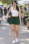 Woman wearing the Forest Green Essential women's athletic shorts with pockets and the Vantacore V emblem – front view