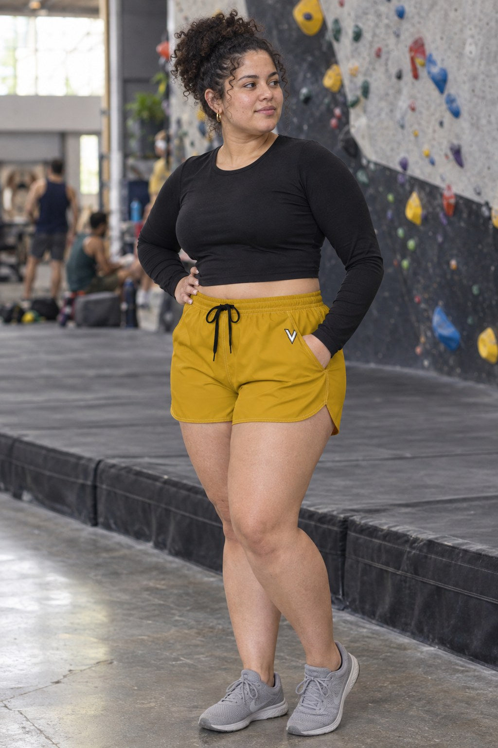 Woman wearing the Mustard Gold Essential women's athletic shorts with pockets and the Vantacore V emblem – three-quarter view showing the side pocket and V emblem