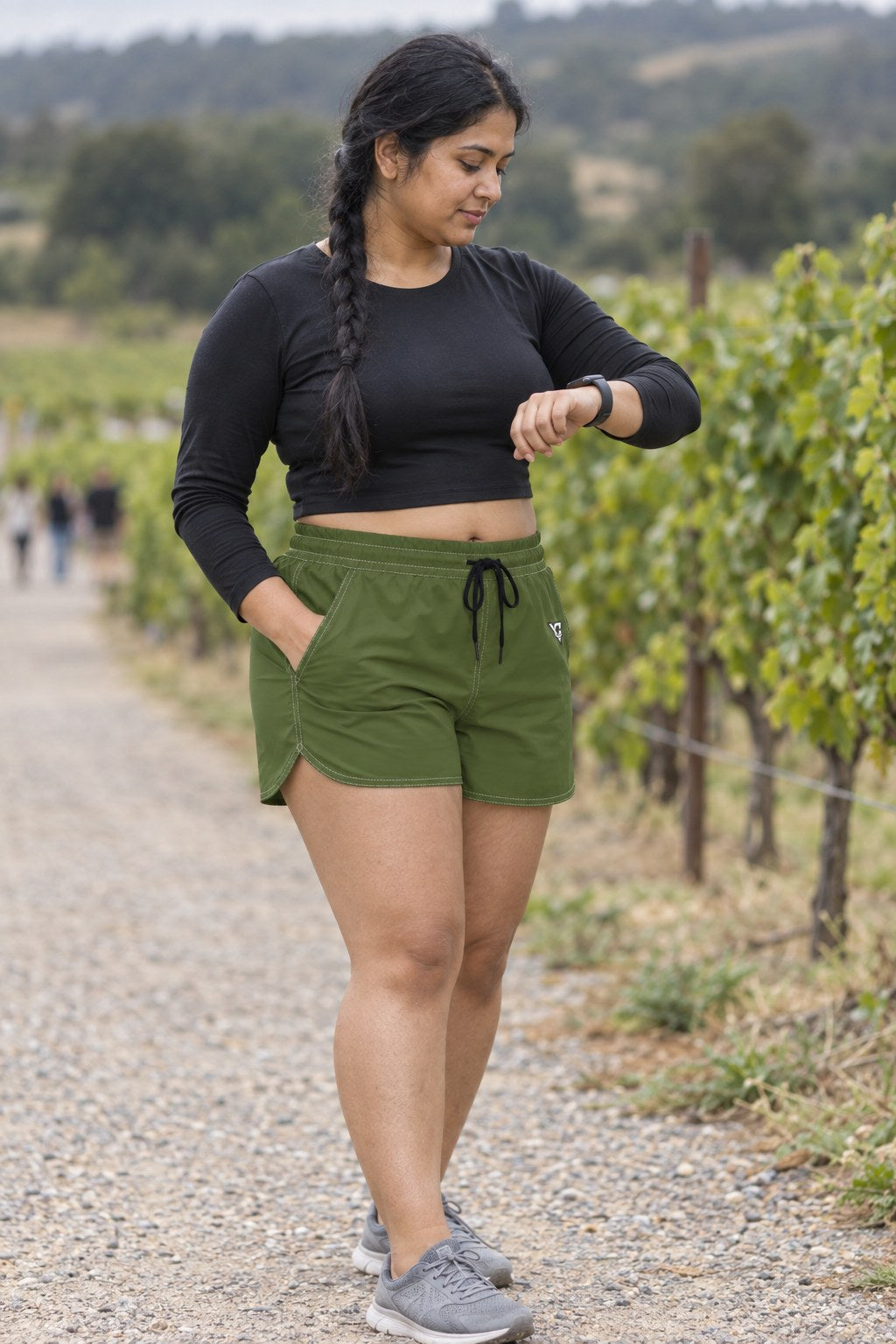 Woman wearing the Olive Green Essential women's athletic shorts with pockets and the Vantacore V emblem – three-quarter view showing the side pocket and V emblem
