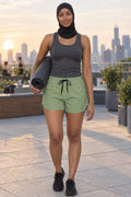 Woman wearing the Sage Green Essential women's athletic shorts with pockets and the Vantacore V emblem – front view