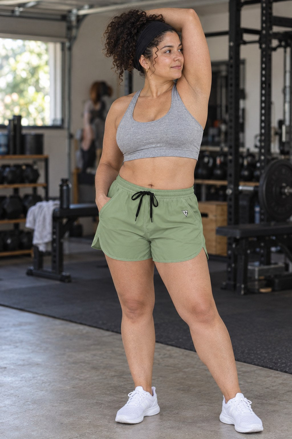 Woman wearing the Sage Green Essential women's athletic shorts with pockets and the Vantacore V emblem – three-quarter view showing the side pocket and V emblem