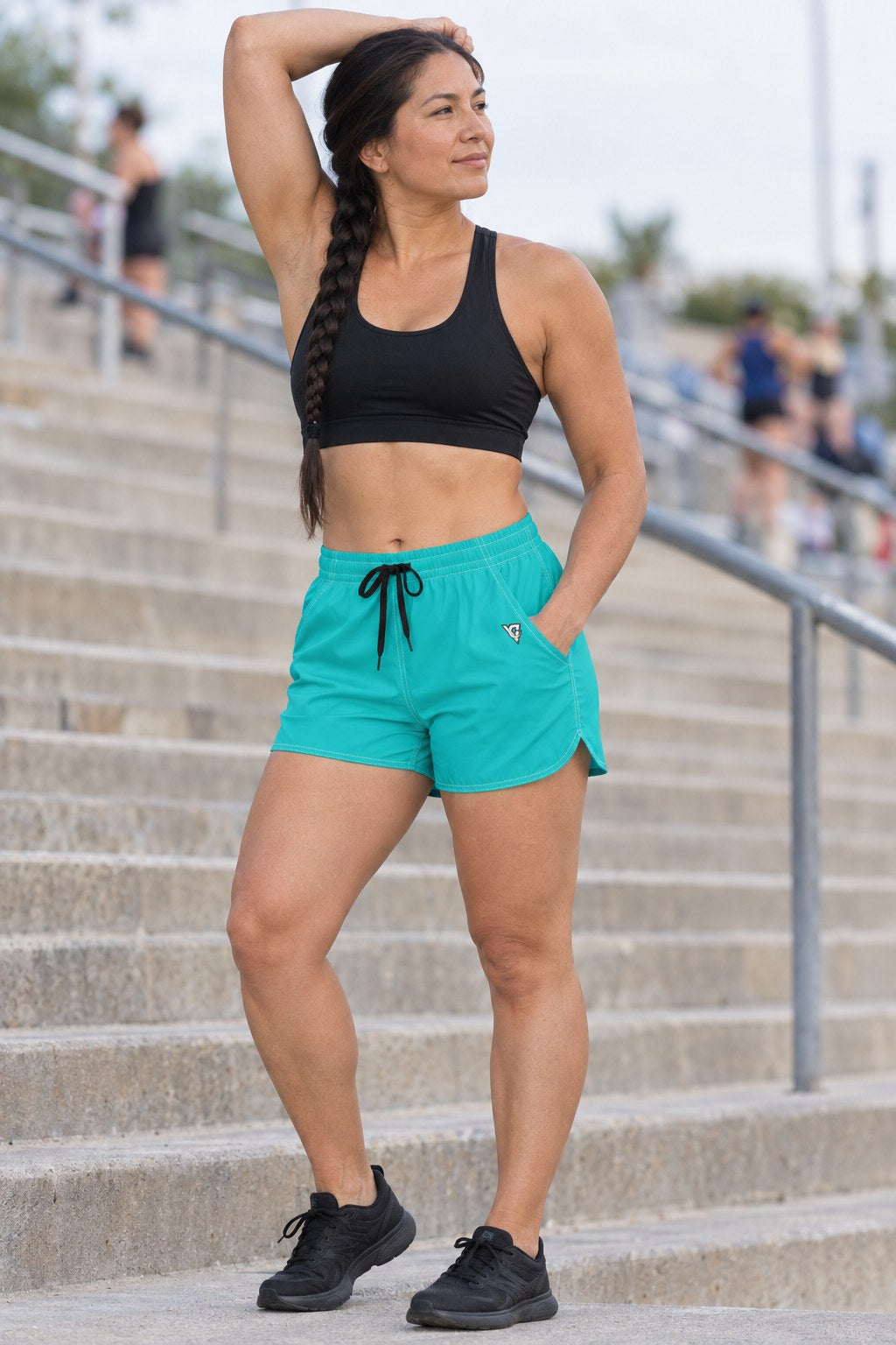 Woman wearing the Turquoise Essential women's athletic shorts with pockets and the Vantacore V emblem – three-quarter view showing the side pocket and V emblem